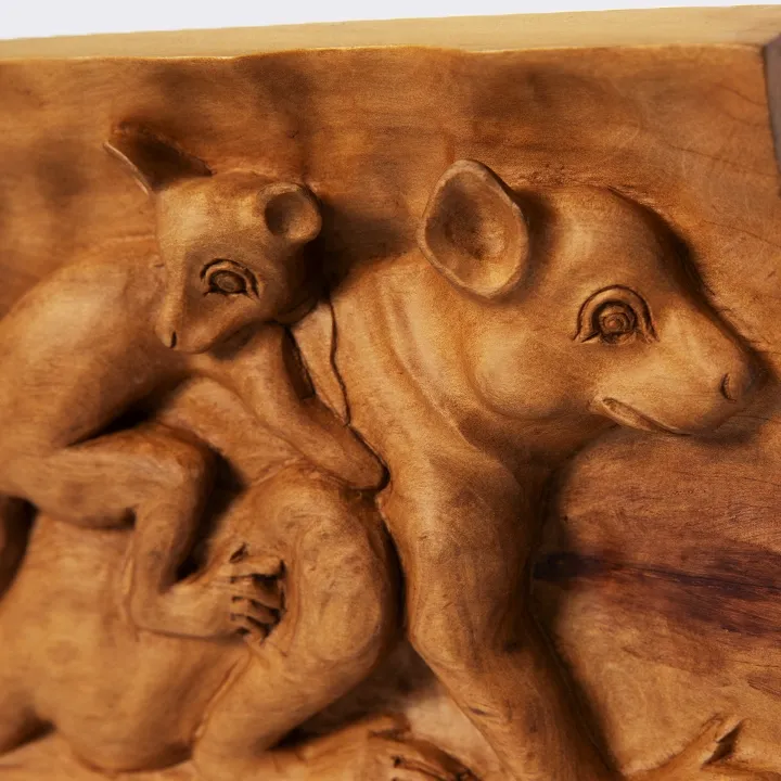 Close-up of the hand-carved wooden panel depicting a baby lemur clinging to its mother, highlighting the warm grain of the exotic wood, the fine details of the carving and the smooth finish.