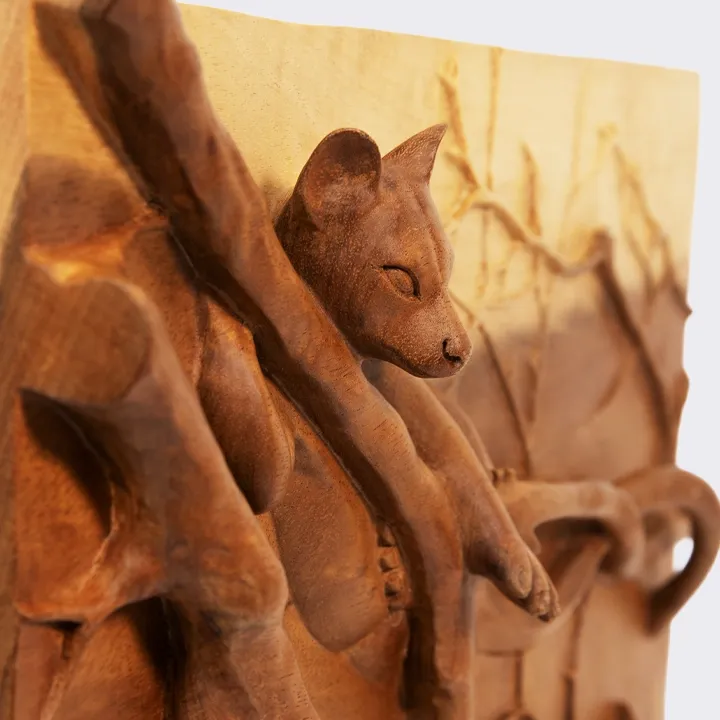Close-up of a hand-carved wooden relief, showing the face of a resting fossa, highlighting the depth of the handcrafted carving, the texture of the wood, the meticulous workmanship and the refined details of the finish.