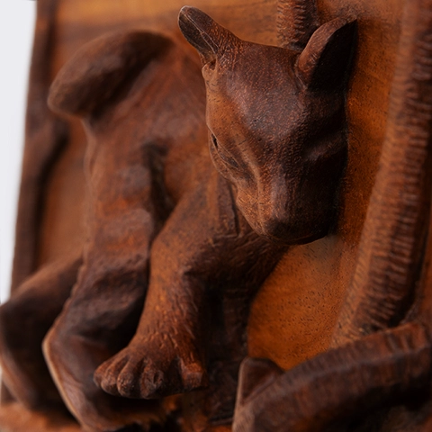 Close-up of a hand-carved wooden relief showing the curious expression of a baby fossa, highlighting the handcrafted texture of the wood and a refined finish.