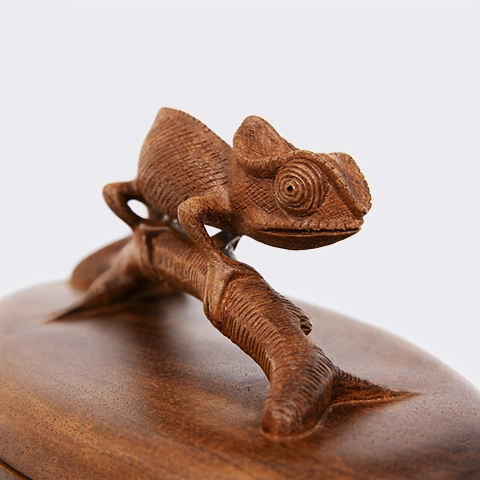 Close-up of a hand-carved wooden handle depicting a chameleon, on a box lid, highlighting the handcrafted texture of the wood and a refined finish.
