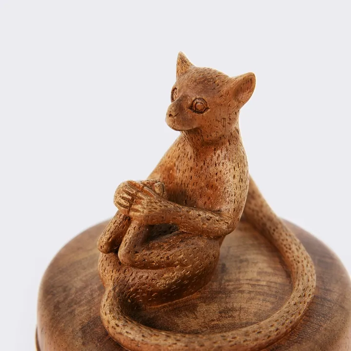 Close-up of a hand-carved wooden lemur sitting on a box lid, highlighting its curled tail and the craftsmanship as well as a refined finish.