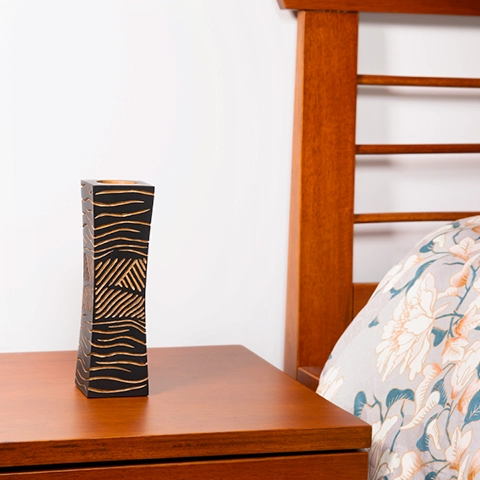 Modern bedroom decor: Elegant carved black wood candlestick placed on a wooden bedside table, next to a patterned cushion.