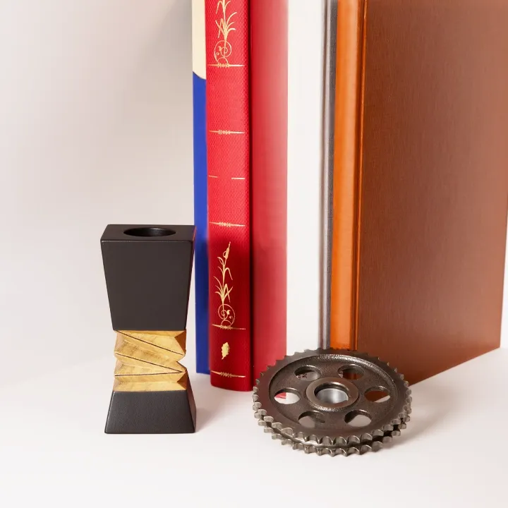 Industrial chic desk accessory: Single black wooden geometric candle holder displayed next to books and vintage gear.