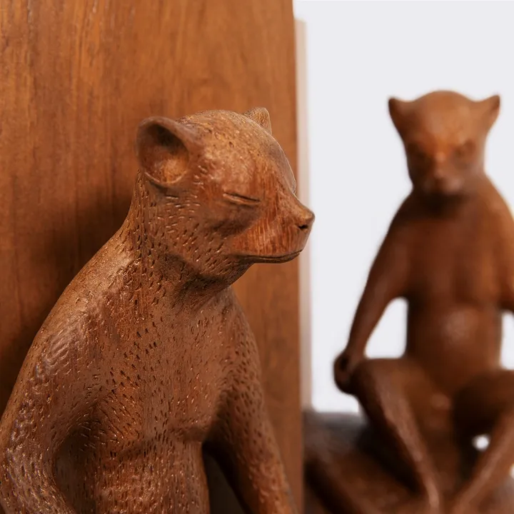 Detail of a sculpture of a lemur sitting on a wooden bookend, showing the texture of the hand-carved fur and a smooth finish.