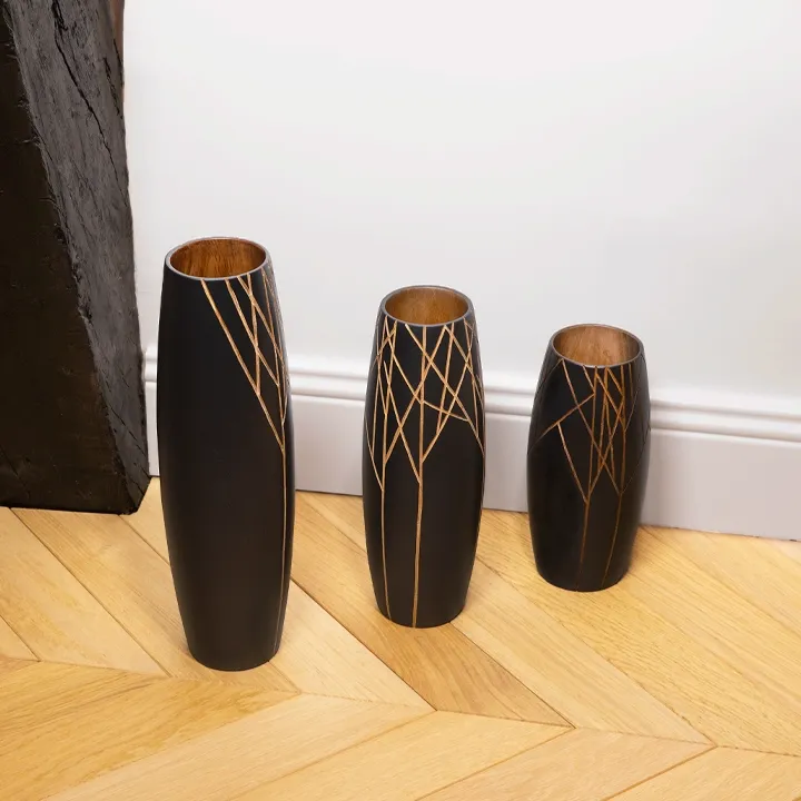 Modern design inspiration: a set of three large black wooden vases arranged on a herringbone parquet floor.