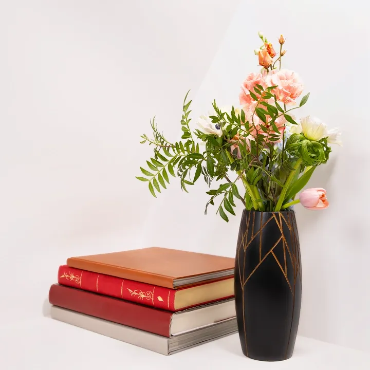 An elegant, handcrafted black wooden vase containing flowers, displayed alongside art books for a refined, contemporary interior.