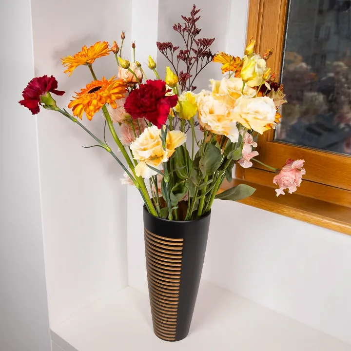 Floral container: a unique black wooden vase, hand-carved and adorned with geometric engravings, holds a colorful bouquet by a window.