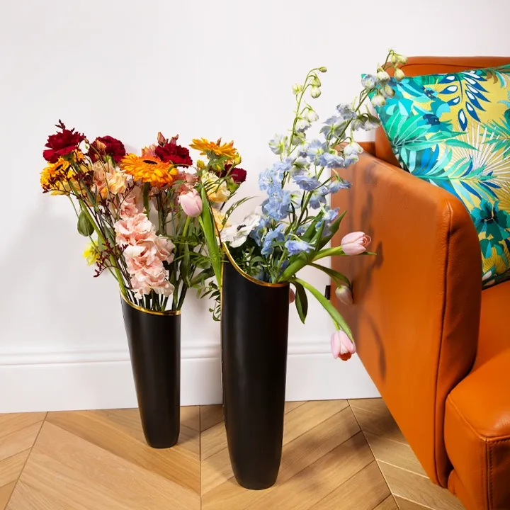 Luxurious floral arrangement: two black architectural vases arranged on a herringbone parquet floor, adorned with vibrant blooms. 