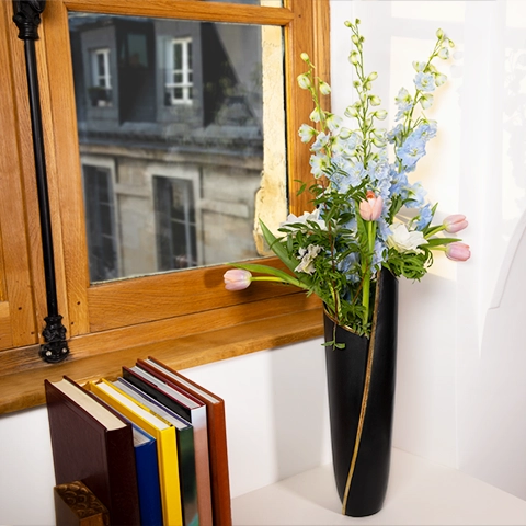 Elegant window display: a matte black Skyscraper vase with a gold trim holds a bouquet. 
