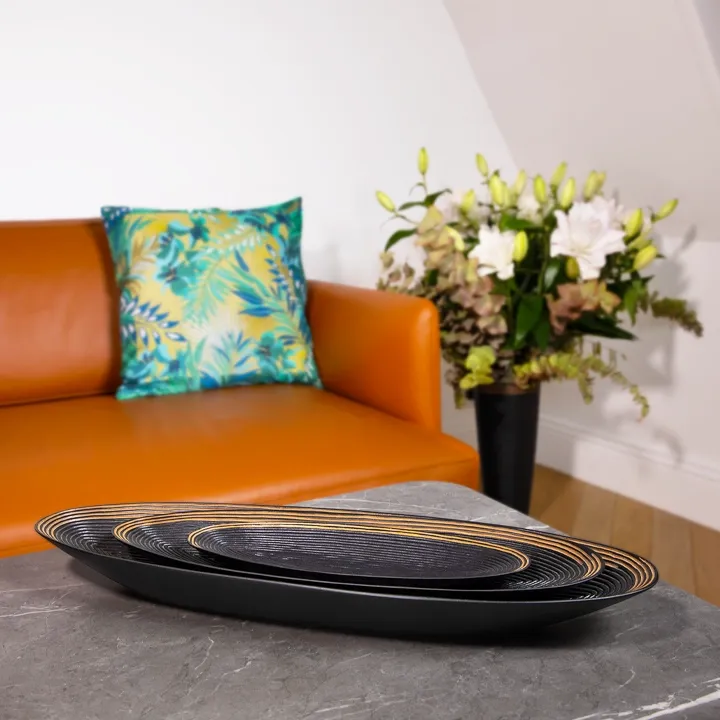 Modern table setting: a set of three nesting oval trays in black wood, displayed on a gray marble coffee table.