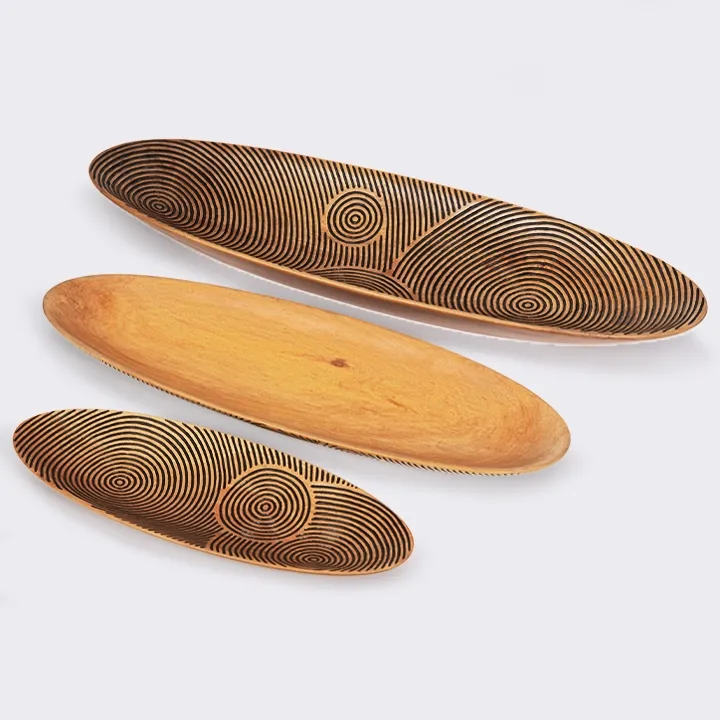 Set of three nesting oval wooden serving trays with black graphic engravings, inspired by traditional Madagascar canoes.