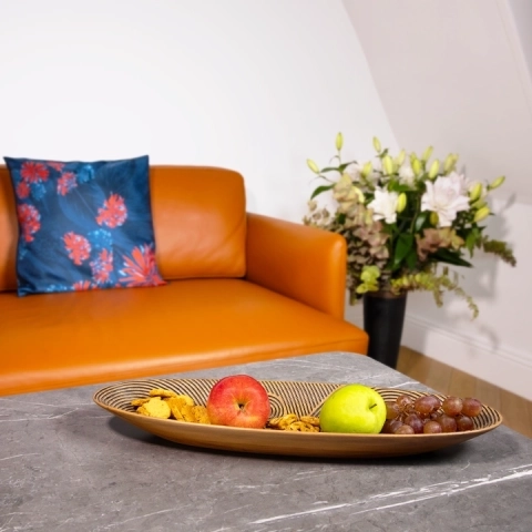 Modern dining table centerpiece: Long boat-shaped wooden fruit bowl displayed on a grey marble table with fresh apples