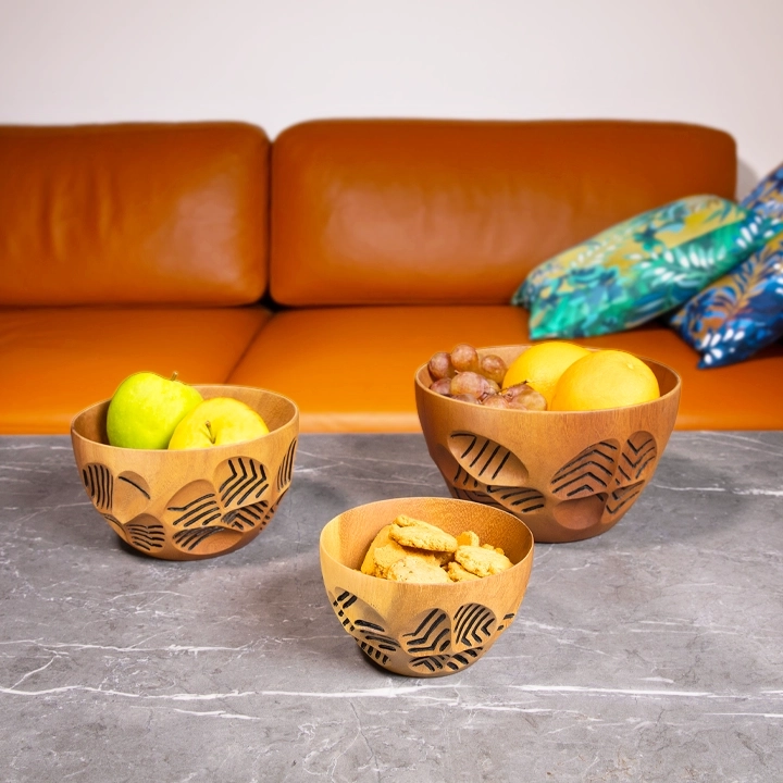 Set of three nesting carved wooden bowls, arranged on a contemporary stone coffee table.