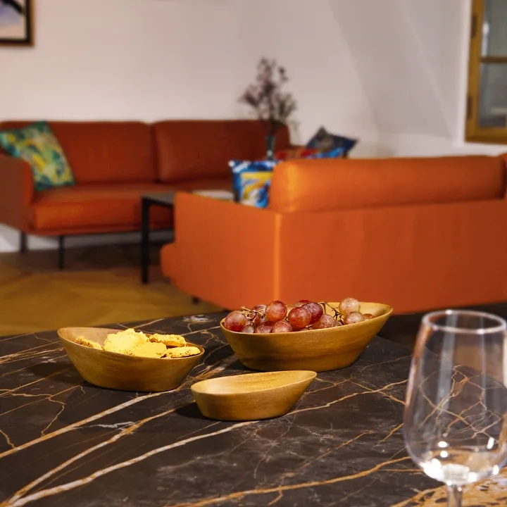 Elegantly set table: a set of nesting sohihy wooden bowls, filled with fruit, on a dark marble dining table.