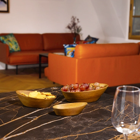Elegantly set table: a set of nesting sohihy wooden bowls, filled with fruit, on a dark marble dining table.